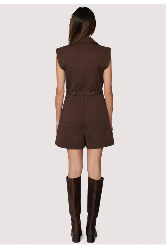 Woman wearing a brown sleeveless dress with a belt and matching knee-high boots on a white background