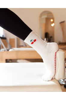  White sock with red cherries design worn by a person sitting on a chair.