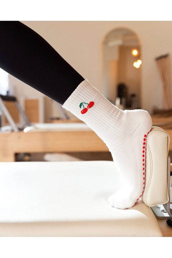 White sock with red cherries design worn by a person sitting on a chair.