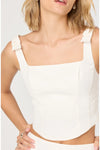 Close-up of woman wearing a white sleeveless top with a bow on the strap on a plain background