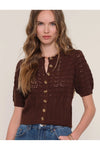 Woman wearing a brown knitted cardigan with gold buttons on a plain background