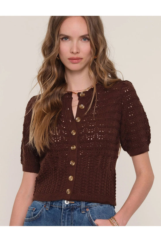 Woman wearing a brown knitted cardigan with gold buttons on a plain background