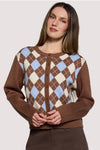 A woman wearing a brown cardigan with an argyle pattern in cream, light blue, and brown, posed against a solid light gray background.