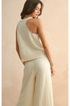 Woman wearing a light-colored sleeveless top and pants against a beige background