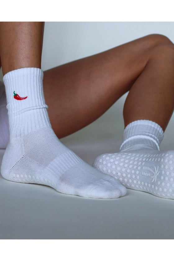 White socks with a chili pepper design on one foot, worn by a person sitting on a light gray surface.