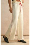 White pants with red stitching and a red drawstring worn by a person on a beige background