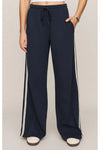 A person wearing navy wide-leg drawstring pants with white side stripes, shown from the waist down against a plain light beige studio background.