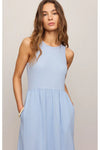 Woman wearing a light blue sleeveless dress against a plain white background. 
