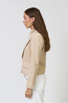 Woman shown from the side wearing a beige blazer and white pants with gold hoops on a white background. 