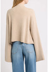 A person shown from the back wearing a light beige cropped knit sweater with long wide sleeves and light blue jeans against a plain light gray studio background.