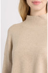 Close-up of a person wearing a soft knit mock-neck sweater in a light warm beige color against a plain light background.