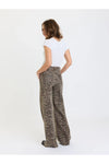 A woman shown from the back wearing high-waisted, wide-leg trousers with a brown and beige leopard print, paired with a white t-shirt, against a plain white studio background.