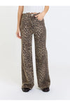 A person wearing high-waisted, wide-leg pants with an allover leopard print pattern in brown, beige, and black, paired with a white top and black shoes, against a plain white studio background.