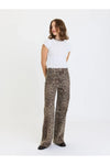 A woman modeling a pair of wide-leg trousers with a brown and beige leopard print pattern, paired with a white ribbed short-sleeve top, against a plain white studio background.