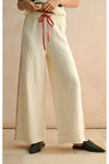 Person wearing wide-leg cream pants with red drawstring and trim on a beige background