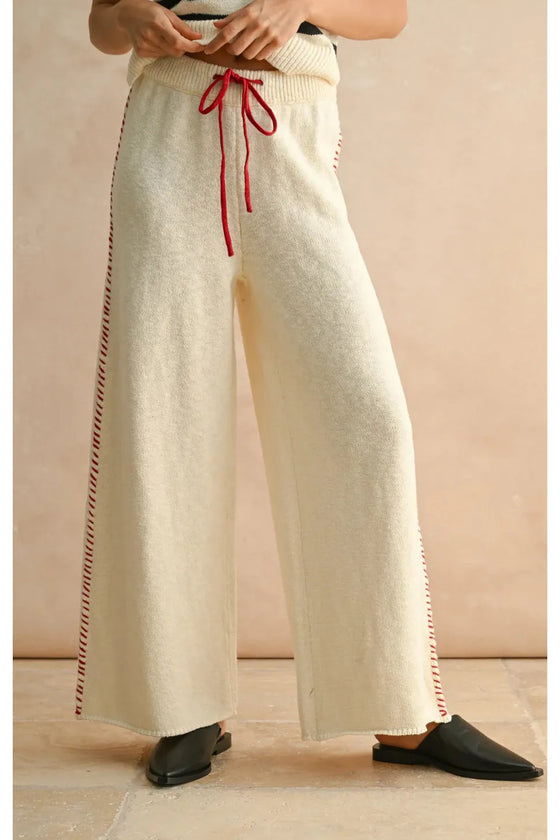 Person wearing wide-leg cream pants with red drawstring and trim on a beige background