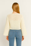 Person wearing a cream knitted sweater and blue jeans on a beige background