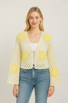 girl wearing blue jeans and with top with a ivory crochet cardigan with yellow flowers on a white background.