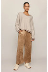A woman modeling a light beige knit sweater and wide-leg tan pants against a plain light gray studio background.