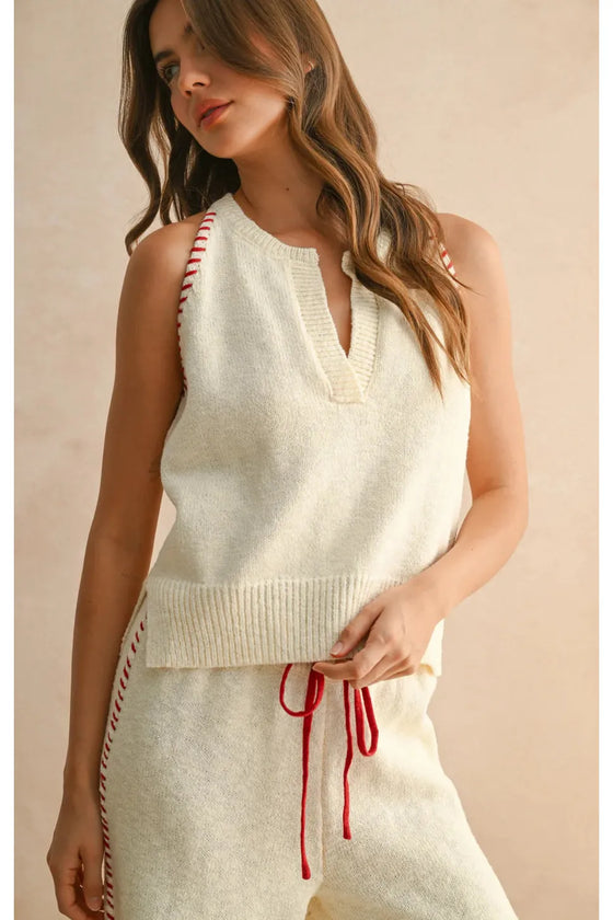 Woman wearing a cream-colored sleeveless top with red accents on a beige background