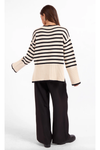 The back of a woman wearing a cream and black horizontally striped ribbed knit sweater and black pants. 