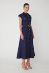 Woman shown from a side view wearing a navy midi dress with a belt and gold buttons on a white background