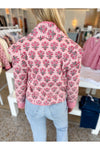 Women shown from behind wearing a pink floral patterned quilted jacket and blue jeans in a store setting. 