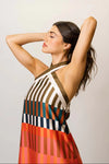 Woman shown from the side wearing a multi-color striped midi dress against a plain background