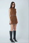 A woman modeling a sleeveless brown mini dress with a silver chain-stitched waist and hem, paired with black knee-high leather boots, against a light gray studio background.