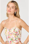 Woman wearing a floral dress with thin straps against a plain background. 