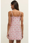 Woman wearing a pink lace-lined slip dress with red heart patterns on a plain background. 