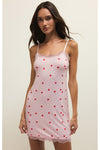 Woman wearing a sleeveless pink slip dress with red heart patterns on a plain background. 