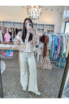 Women taking a mirror selfie in a short sleeve ivory blouse with red, pink and green embroidered pattern and ivory jeans with white sneakers. 