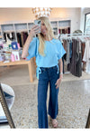 Woman taking a mirror selfie wearing a light blue short sleeve top and dark blue jeans in a clothing store.