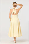 Woman shown from behind wearing a light yellow midi dress with a bow halter neck detail on a white background. 