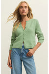 Woman wearing a long sleeve green button down cardigan and blue jeans against a plain background