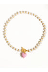 Pearl necklace with a pink heart charm on a white background. 