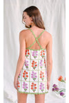 Woman shown from behind wearing a white mini floral dress with green crossed straps on a white background 