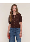 Woman wearing a brown knitted cardigan and blue jeans against a plain background