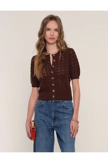  Woman wearing a brown knitted cardigan and blue jeans against a plain background