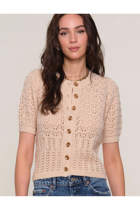 Woman wearing a beige crochet cardigan with buttons on a plain background