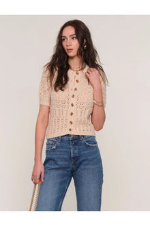  Woman wearing a beige crochet top and blue jeans against a plain background