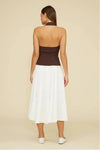 Woman wearing a two-tone dress with brown top and white skirt on a beige background