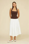 Woman wearing a brown top and white skirt on a beige background